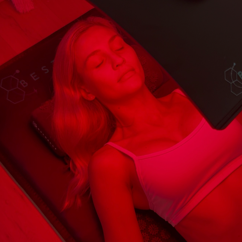 Candice under red light lamp while laying on PEMF mat with acupressure pad